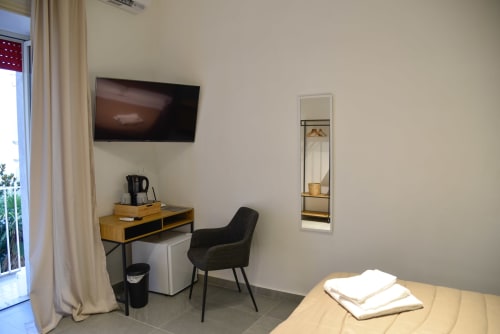 Camera moderna all'Onde Del Mare di Napoli con scrivania, TV a schermo piatto, comoda poltrona e specchio con vista sul giardino su tonalità beige