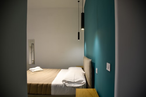 Camera moderna presso Onde Del Mare, BnB a Napoli, con letto dalle lenzuola bianche, parete azzurra, illuminazione a sospensione e