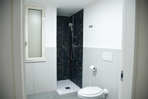 Bagno moderno con doccia rivestita in piastrelle scure, wc bianco e finestra all'hotel Onde Del Mare di Napoli
