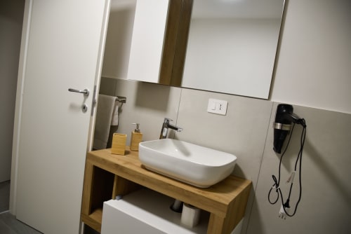 Bagno moderno all'Onde Del Mare di Napoli con lavabo in ceramica bianca su mobile in legno, specchio e servizi nella Camera Deluxe