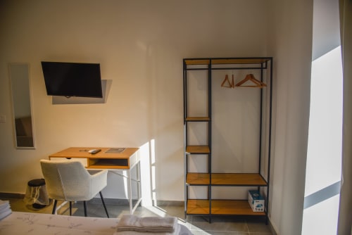 Camera da letto moderna con scrivania in legno, sedia, TV a parete, armadio metallico con ripiani e luce naturale presso Onde