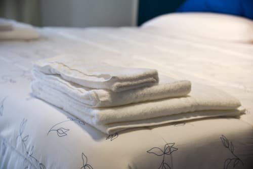 Asciugamani bianchi e beige piegati impilati su una coperta decorata presso Onde Del Mare, un affittacamere sul lungomare di Napoli.