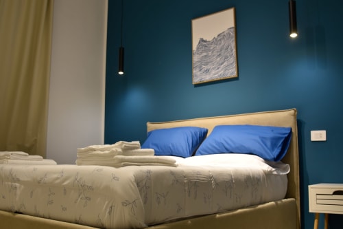 Camera da letto moderna con parete azzurra, letto in legno, cuscini blu e biancheria bianca presso l'hotel boutique Onde Del Mare