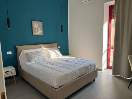 Camera moderna all'Onde Del Mare con parete in turchese, letto beige, luci a sospensione e accesso alla vista mare a Napoli