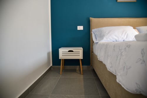 Camera moderna dell'Onde Del Mare B&B a Napoli con parete blu teal, letto color sabbia, cuscini bianchi e comodino in legno