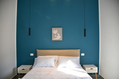 Camera da letto moderna con parete teal, testiera color sabbia, lampadari a sospensione e arredi minimalisti a Onde Del Mare, Napoli