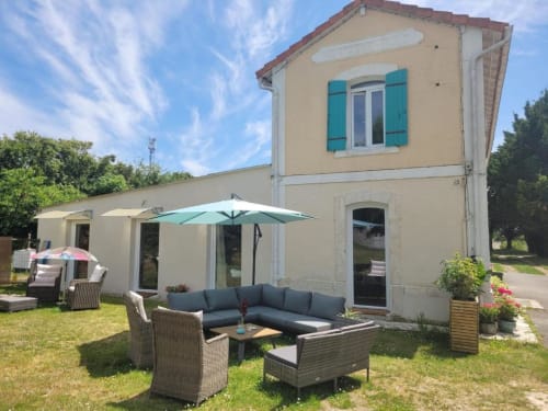 Domaine de la Gare M garden terrace with seating, umbrellas, and cream villa in Mortagne-sur-Gironde