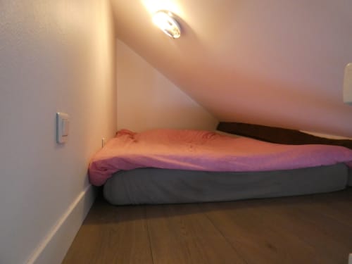Chambre mezzanine cosy à l'appartement Sci Ludji à Nanterre avec éclairage chaleureux et linge de lit coloré sur parquet