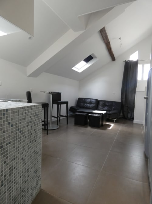 Loft moderne à Nanterre avec canapé en cuir noir, coin repas, puits de lumière et carrelage gris foncé