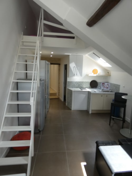 Appartement mezzanine moderne à Nanterre avec escalier blanc, kitchenette, sol foncé et puits de lumière