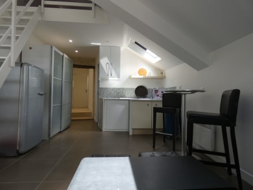 Cuisine moderne avec réfrigérateur inox, armoires blanches et cuisinière noire dans un appartement à mezzanine à Nanterre