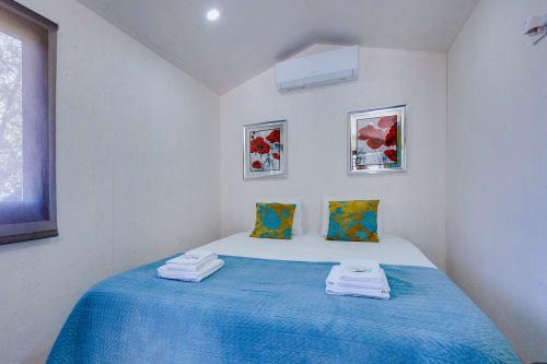 Quarto moderno na Arrabia Guest Houses com roupa de cama azul, almofadas amarelas, obra de arte com flores vermelhas, ar-condicionado e glamping à beira do rio