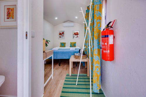 Interior da cabana de glamping em Arrabia Guest Houses com cama azul, cortina estampada em amarelo, piso de madeira e extintor