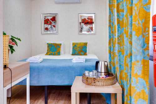 Quarto colorido da Arrabia Guest Houses Glamping com cama azul, almofadas amarelo-verde, arte floral e cortinas estampadas