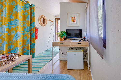 Quarto colorido na Arrabia Guest Houses com cortinas azuis e amarelas, escrivaninha com TV, frigobar branco e tapete listrado