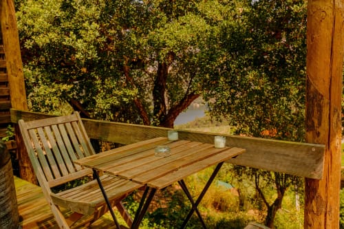 Mesa e cadeira de madeira na varanda da Glamping Arrabia Guest Houses em Castelo de Paiva, rodeadas por exuberante vegetação
