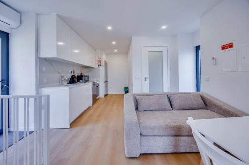 Studio moderno de planta aberta na Arrabia Guest Houses com sofá cinzento, cozinha branca, pisos em madeira e decoração contemporânea
