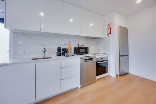 Cozinha moderna branca da Casa Bernardo nas Casas de Hóspedes Arrabia, Portugal, com eletrodomésticos em aço inoxidável e mármore