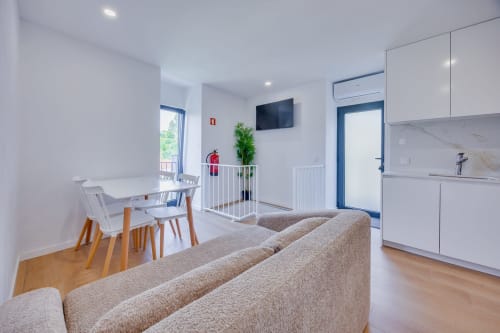 Espaço de estar moderno e integrado na Casa Bernardo, Arrabia Guest Houses, com sofá bege, mesa de jantar branca, cozinha e TV