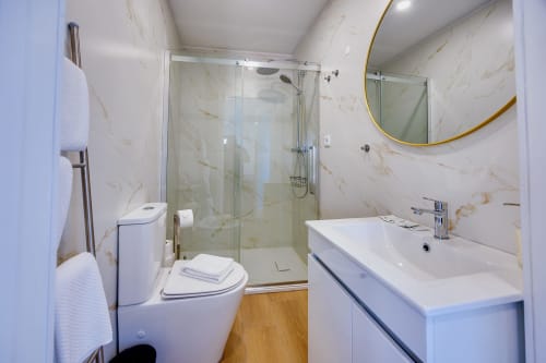 Banheiro moderno na Casa Bernardo em Arrabia Guest Houses com paredes em mármore, chuveiro de vidro, cuba branca e espelho redondo