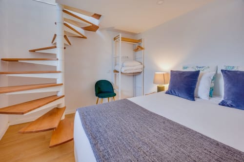 Quarto moderno na Arrabia Guest Houses com escada flutuante em madeira, cama queen com almofadas azuis e móveis contemporâneos