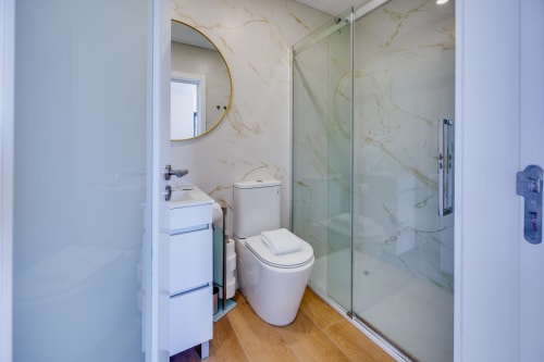 Banheiro moderno na Arrabia Guest Houses com paredes em mármore, chuveiro em vidro, pia e sanitário brancos, e piso em madeira
