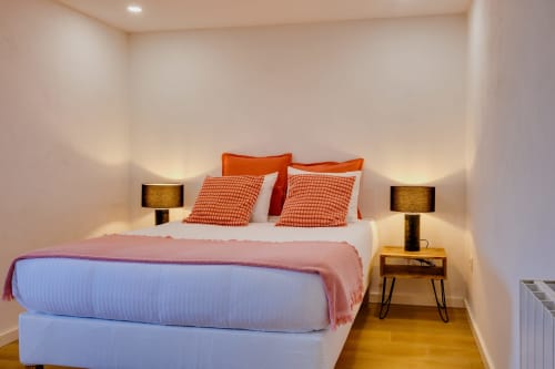 Quarto moderno na Arrabia Guest Houses com almofadas laranja, roupa de cama branca, mesas de cabeceira em madeira com luminárias douradas e ambiente acolhedor