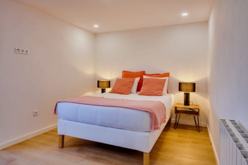 Quarto moderno na Arrabia Guest Houses com cama branca, roupa de cama laranja, criados-mesas geminados com luminárias, piso de madeira e ambiente aconchegante