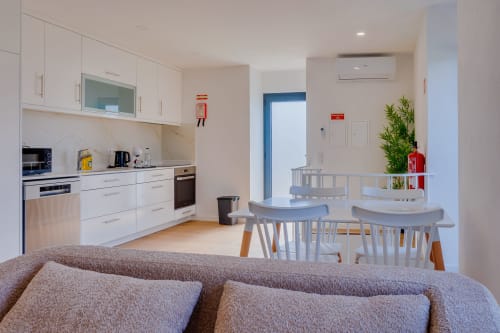 Cozinha e sala de jantar modernas integradas na Arrabia Guest Houses com móveis brancos, cadeiras de jantar e área de estar acolhedora