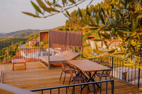 Terraço com deck de madeira nas Casas de Hóspedes Arrabia, com mesa de jantar, espreguiçadeira, ramos de oliveira e vista para colinas florestadas em Castelo