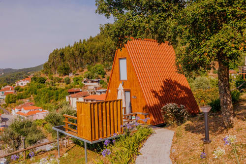 Cabana de glamping laranja na Arrabia Guest Houses em Castelo de Paiva, Portugal, rodeada por árvores verdes e vistas da aldeia