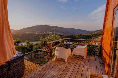 Deck de madeira com cadeiras brancas com vista para o vale do rio e montanhas na Glamping Arrabia Guest Houses em Castelo de Paiva,