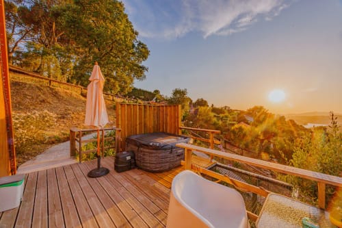 Terraço de glamping das Casas de Hóspedes Arrabia com banheira de hidromassagem, guarda-sol e vista para o rio ao pôr do sol em Castelo de Paiva