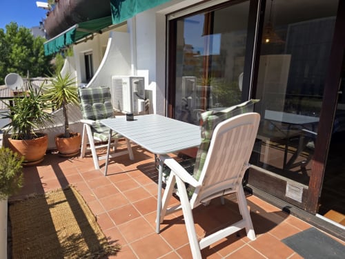 Terrasse ensoleillée avec table à manger, chaises, plantes en pots et accès à un studio à Roses près de la plage