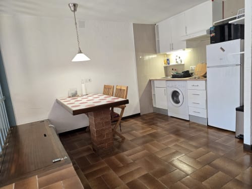 Petite cuisine douillette et coin repas à Roses avec électroménagers blancs, colonne en brique, table en bois et luminaires suspendus