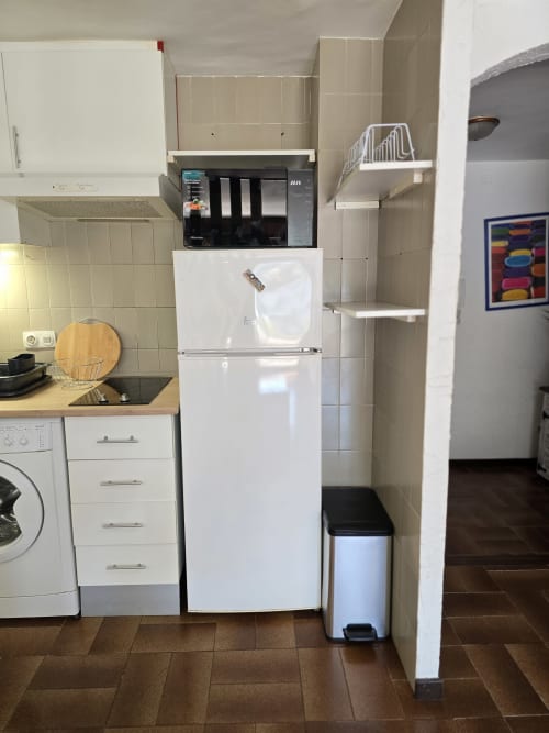 Cuisine compacte de studio à Roses avec réfrigérateur blanc, plaque de cuisson et appareils modernes près de la plage