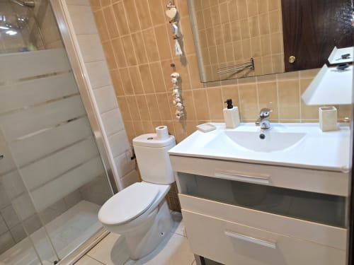 Salle de bain moderne de l'appartement Roses avec meuble-lavabo blanc, toilettes et douche carrelée près de la plage