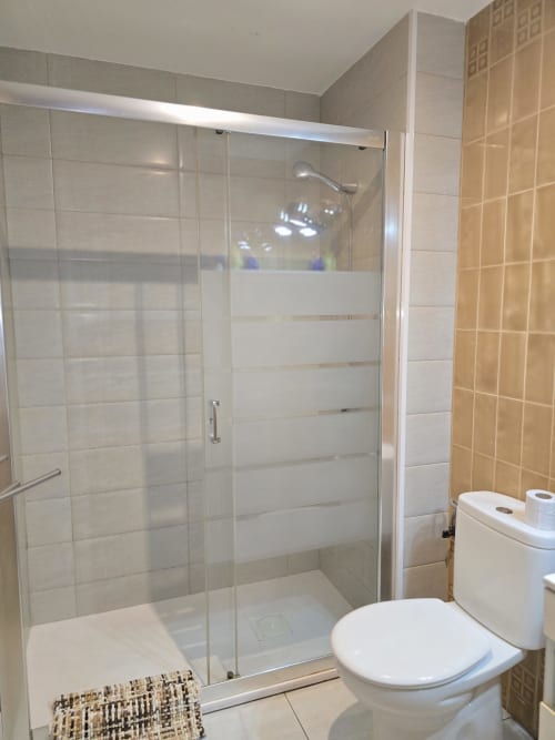 Salle de bain moderne avec douche à l'italienne, toilettes blanches et carrelage beige dans un appartement de vacances près de la plage à Roses