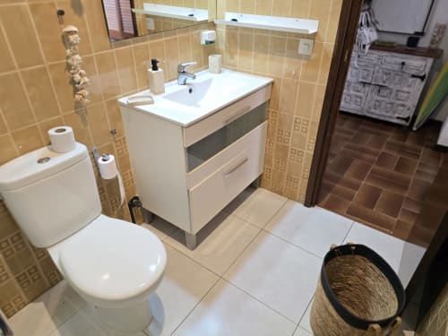 Salle de bain moderne dans un appartement à Roses avec vanité blanche, toilettes et carrelage beige près de la plage