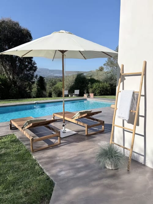 Villa de luxe avec piscine à Grasse, transats en bois, parasol crème, vue montagne et bâtiment blanc
