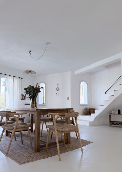 Salle à manger moderne de la villa de Grasse avec table en bois, chaises tressées, murs blancs, fenêtres cintrées et vue sur les montagnes