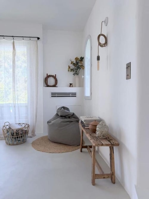 Chambre minimaliste avec pouf gris, banc en bois, plante en pot, miroir et accents de corde à la villa de Grasse