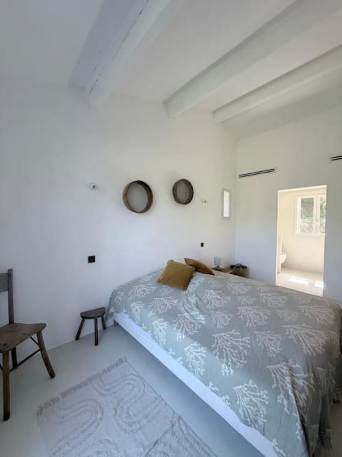 Chambre moderne avec poutres apparentes, lit queen-size à literie motifs, décoration murale circulaire et salle de bains attenante à Grasse