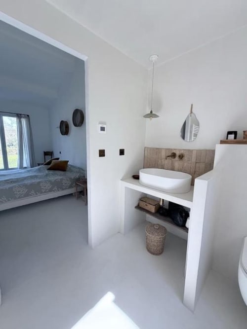 Salle de bain moderne de villa à Grasse avec vasque blanche, miroir avec cadre bois, luminaires suspendus et vue ouverte sur chambre