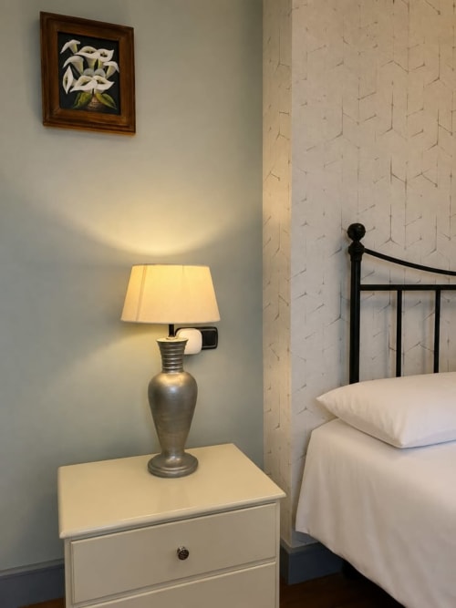 Elegante dormitorio en Casa Señorial Sasueta con mesita de noche blanca, lámpara de latón y cuadro floral enmarcado en San Sebastián.
