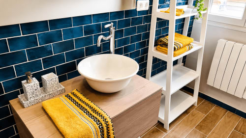 Salle de bains moderne avec lavabo rond blanc, dosseret en carrelage bleu foncé, meuble en bois et touches jaunes à la villa Ô de Mer à Sangatte