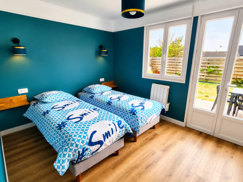 Chambre twin moderne aux murs bleu-vert, literie bleue, lits en bois et portes vitrées donnant sur le jardin à la villa Ô de Mer, Sangatte