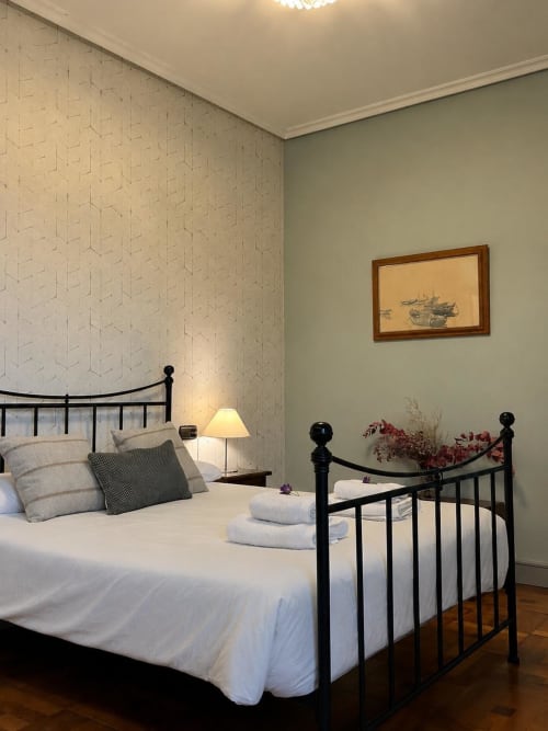 Elegante dormitorio en Casa Señorial Sasueta de San Sebastián con cama metálica negra, papel pintado estampado y arte náutico.