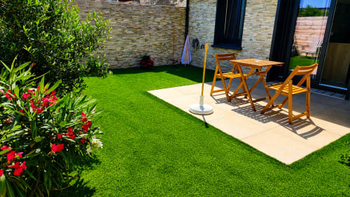 Jardin moderne de la villa Ô de Mer à Sangatte avec gazon synthétique, mobilier en bois et fleurs rouges près de la plage