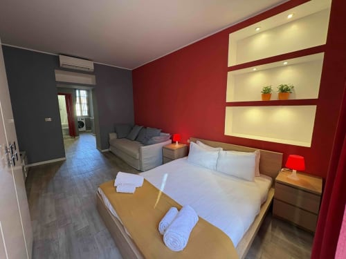 Camera da letto Modern Milano con pareti rosse, letto matrimoniale, divano e scaffali illuminati. Hotel Urban ESCAPE.